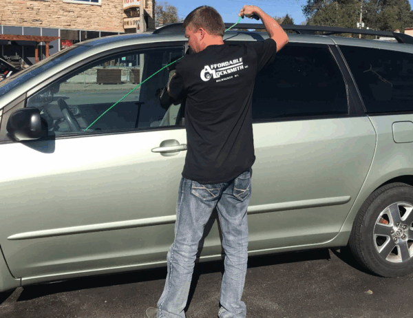 Locksmith unlocking a car door using a long arm tool
