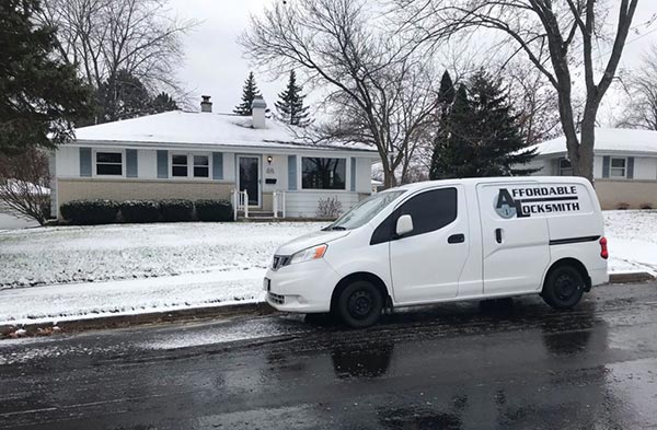A white Affordable Locksmith van is parked on a snowy street outside a residential home.