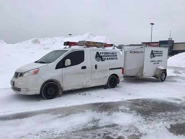 An Affordable Locksmith van with a connected trailer on a snow-covered road.